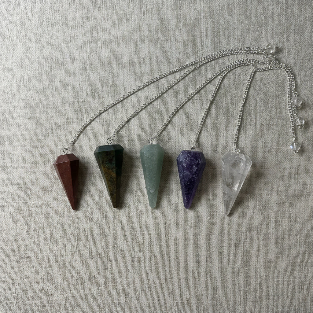Five crystal pendulums on a neutral fabric surface