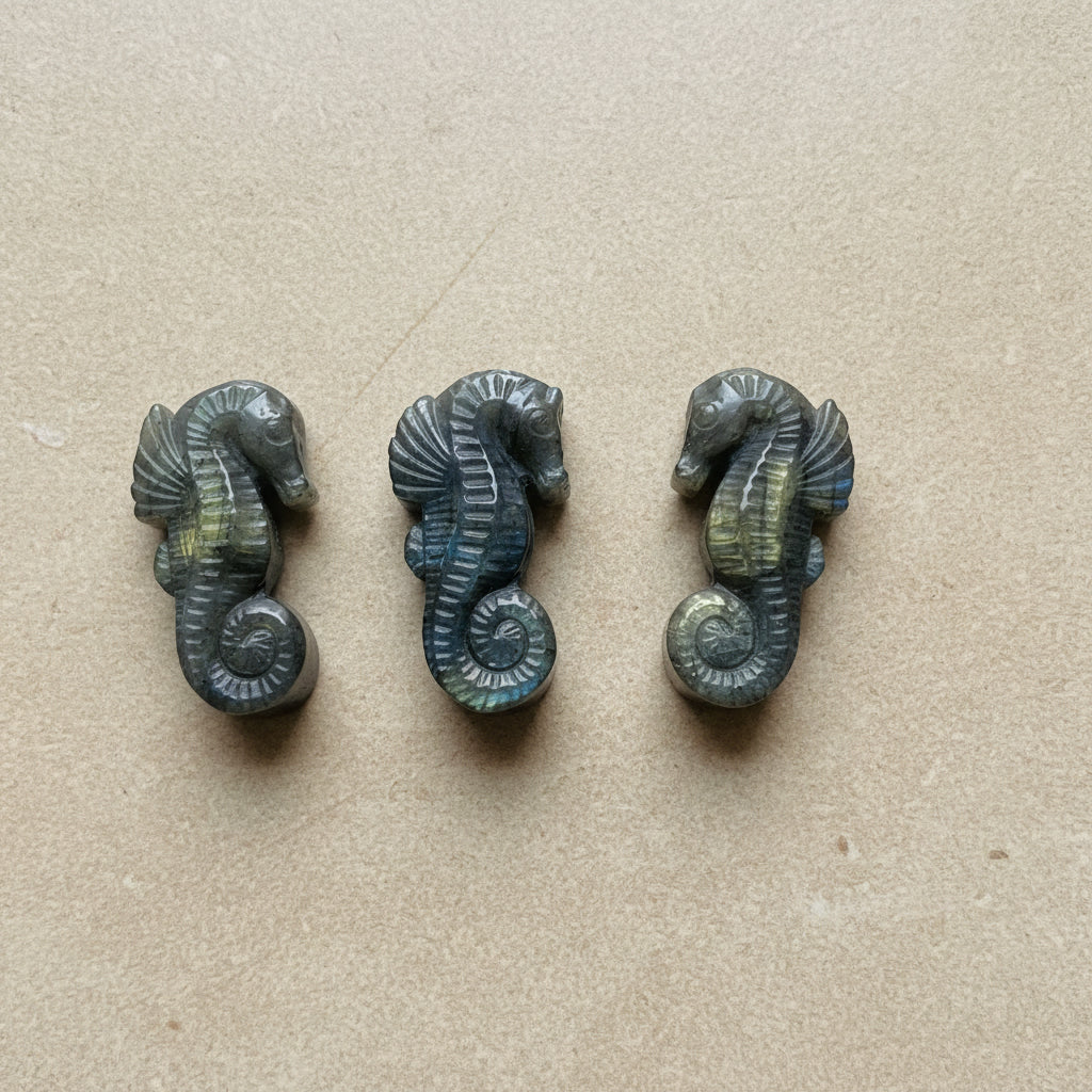 Three labradorite seahorse figurines on a tan background