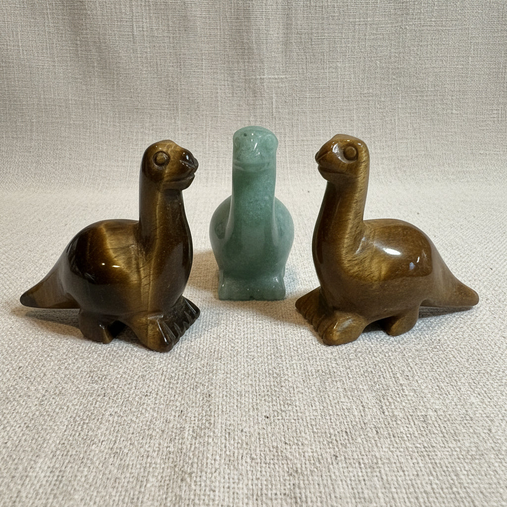Three stone dino figurines on a white surface with a light gray background