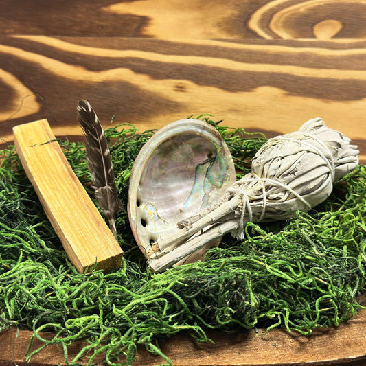Decorative items including a shell, feather, and wooden block on a bed of green moss with a wooden background.