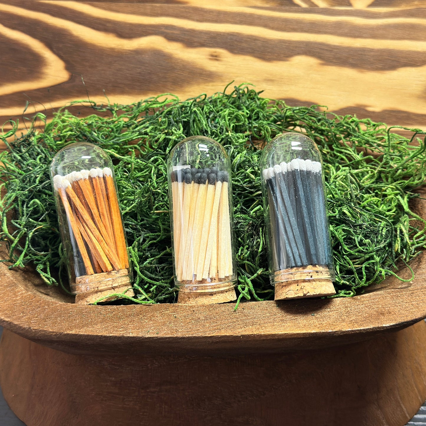 Three glass containers with matches on a wooden stand with grass