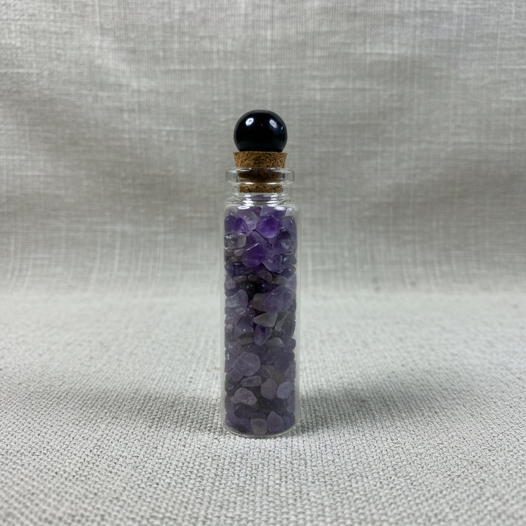 Small glass bottle with purple crystals on a fabric surface