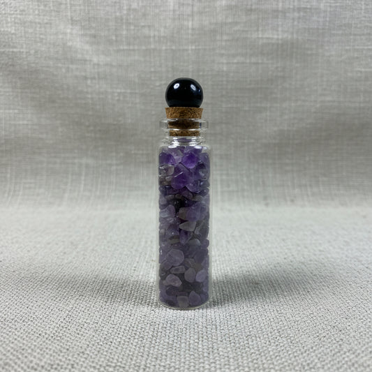 Small glass bottle with purple crystals on a fabric surface