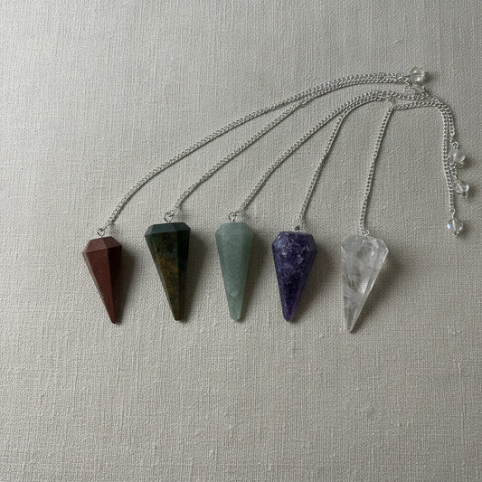 Five crystal pendulums on a neutral fabric surface