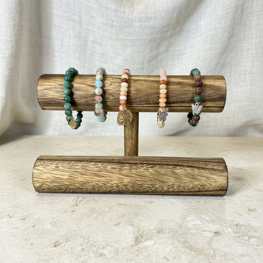 Wooden bracelet holder with beaded bracelets against a white wall.