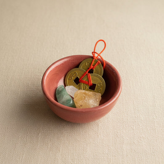 Mauve dish with Chinese coins and a crystal on a light fabric surface