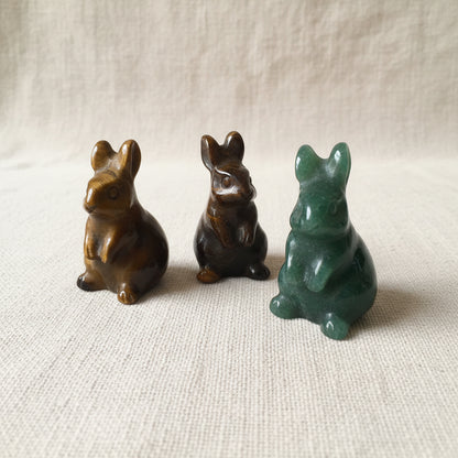 Three stone Rabbit figurines on a tan fabric background