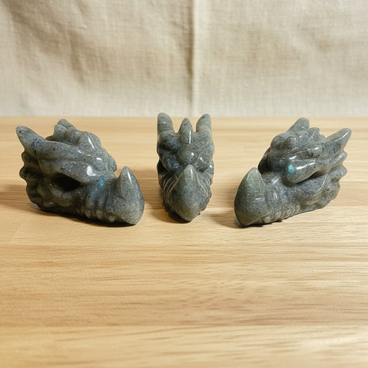 Three stone carvings of dragon heads on a wood background

