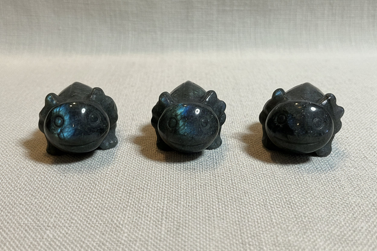 Three dark gray stone carvings of animals on a white surface