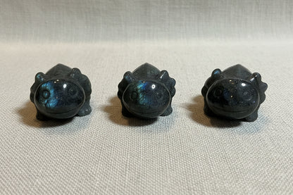 Three dark gray stone carvings of animals on a white surface