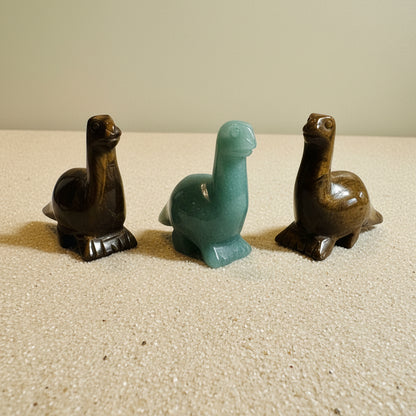 Three stone carvings of dinos on a tan background