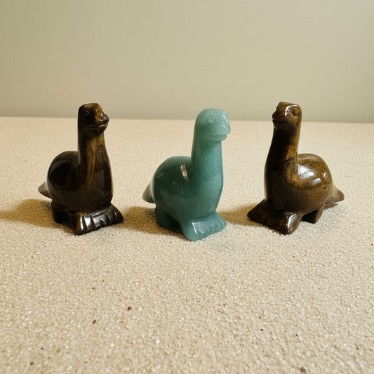 Three stone carvings of dinos on a tan background