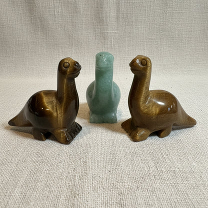 Three stone dino figurines on a white surface with a light gray background